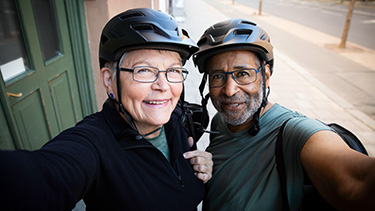 Man and a woman wearing bike helmets smiling at camera.