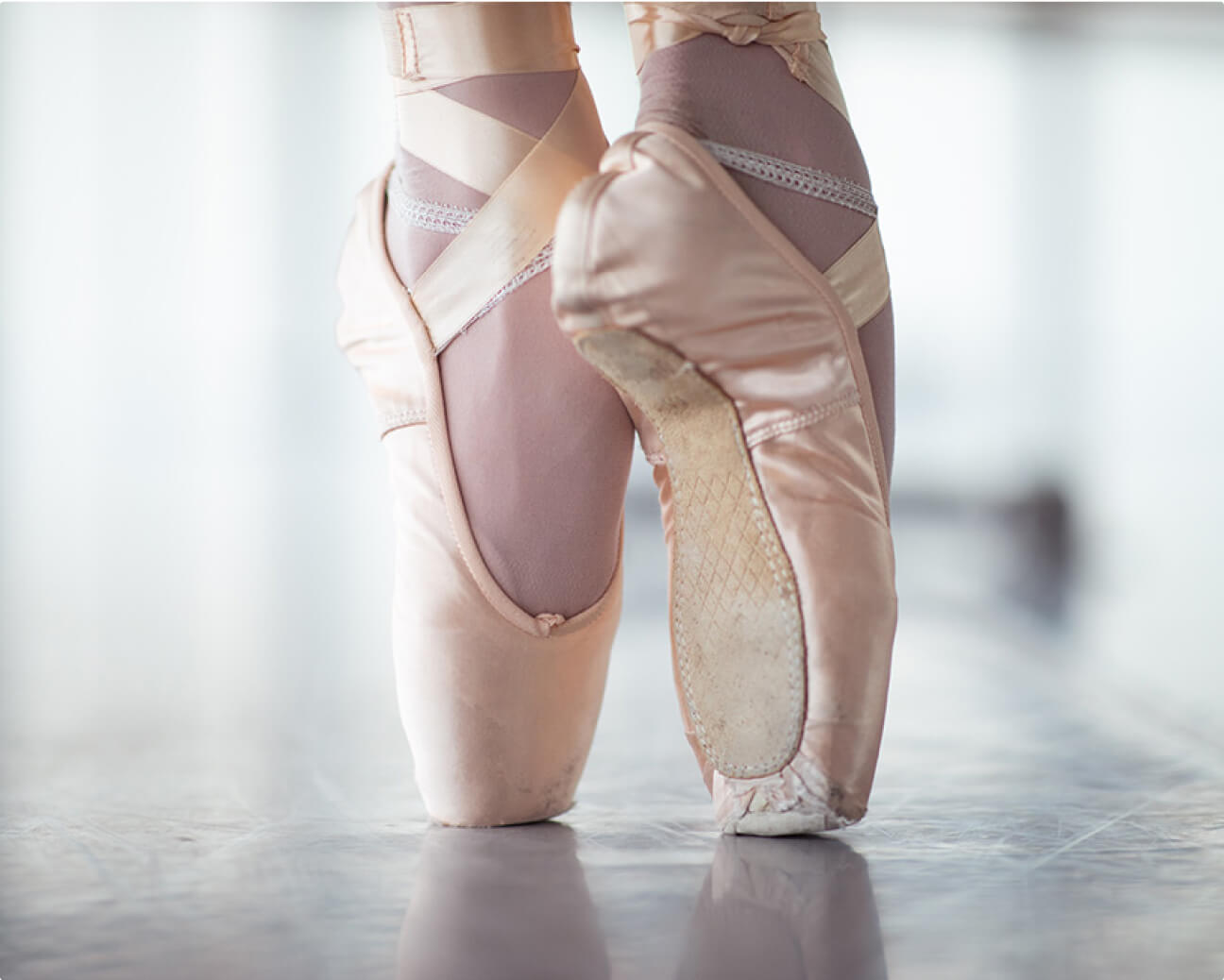 A closeup of a ballerina's feet in light pink shoes, up on toes.
